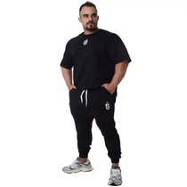 Homem vestindo conjunto de moletom preto fitness com tênis esportivo e logo branco, fundo branco.