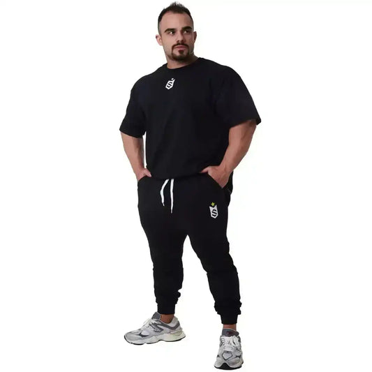 Homem vestindo conjunto de moletom preto fitness com tênis esportivo e logo branco, fundo branco.