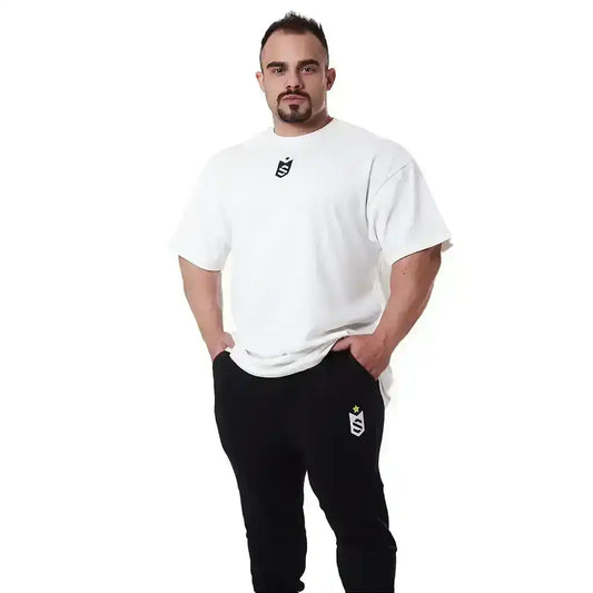 Homem musculoso vestindo camiseta branca e calça preta fitness com logo, fundo branco