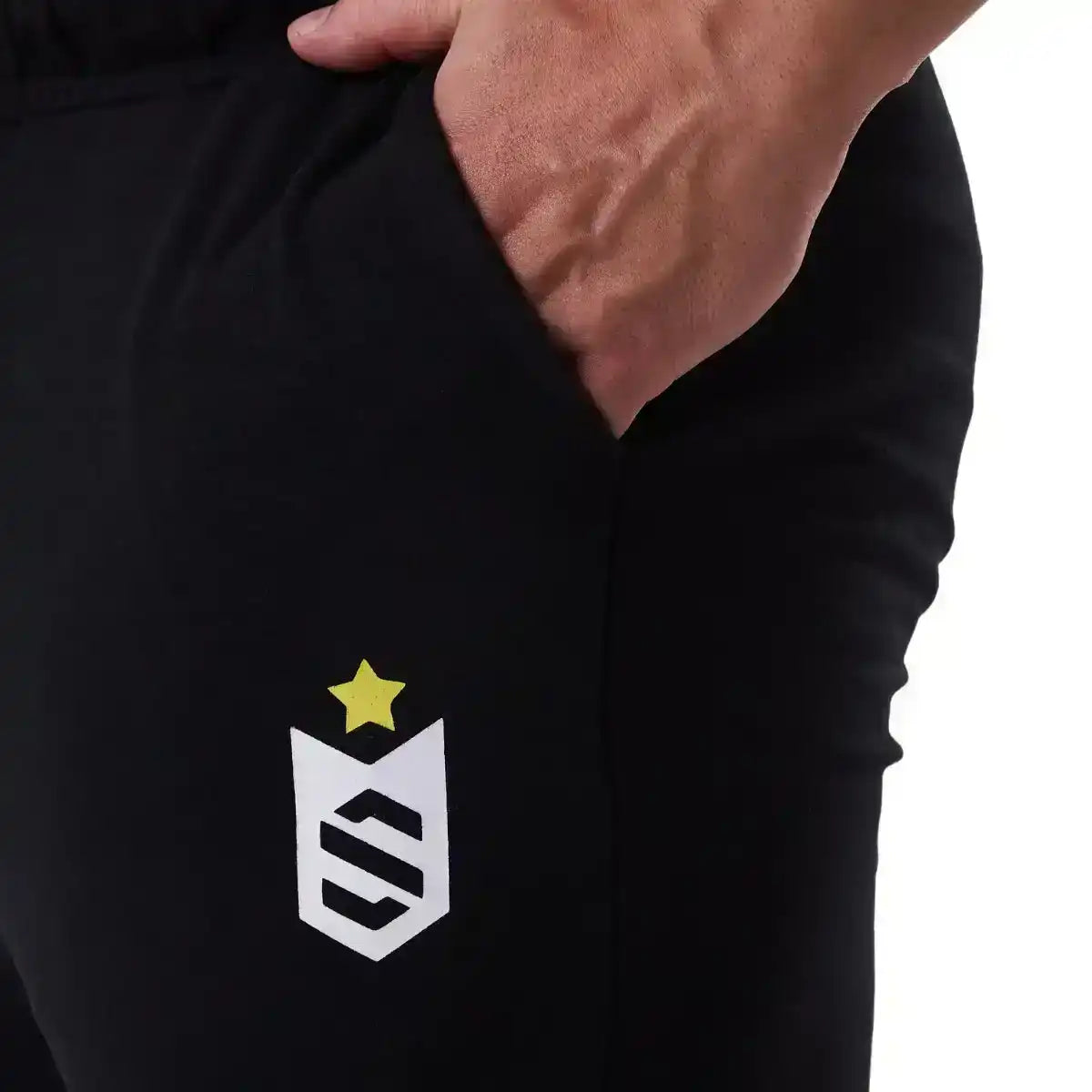 Calça preta fitness masculina com bolso e estampa de estrela e escudo, close na mão no bolso.